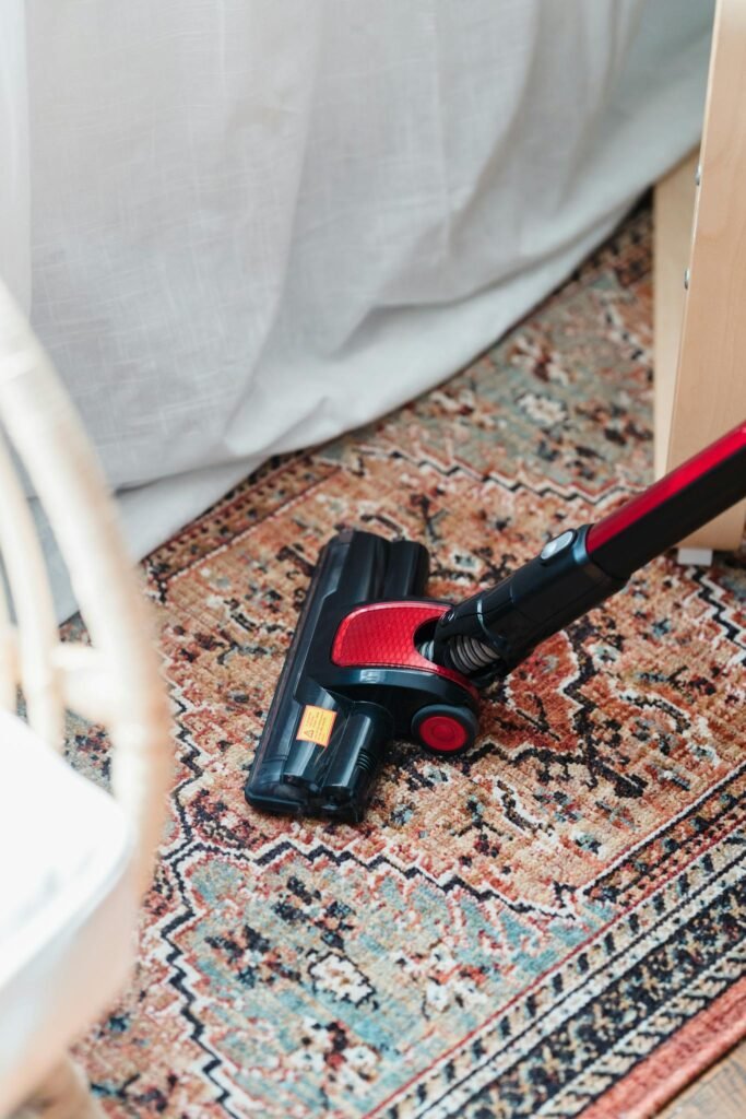 A red and black vacuum cleaner on a vibrant patterned carpet indoors, showcasing home cleaning essentials.